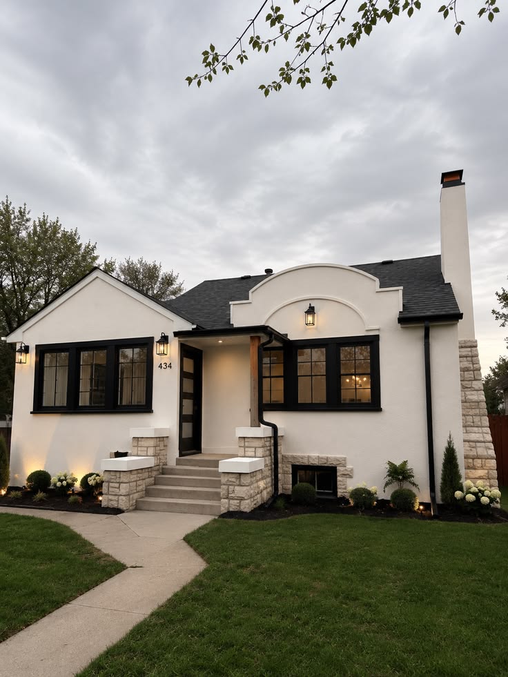 White painted-brick bungalow with black windows and stone porch at twilight